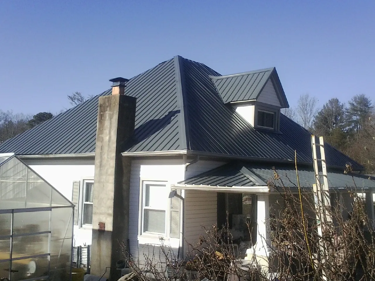 Dark blue standing seam metal roof on a white farmhouse with dormer — Slate & Tile Roof Repair by Roofing Brothers in Blodgett