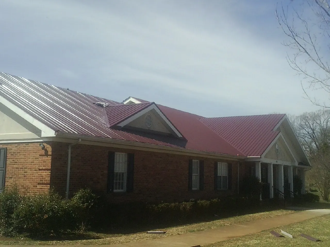 Red metal roof with gabled entries on a long brick building, from a Hail Damage Roof Repair job in Blodgett