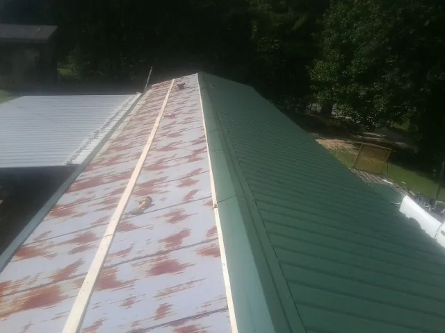 Old rusted panels beside newly installed green metal roofing — Wind Damage Roof Repair by Roofing Brothers in Blodgett