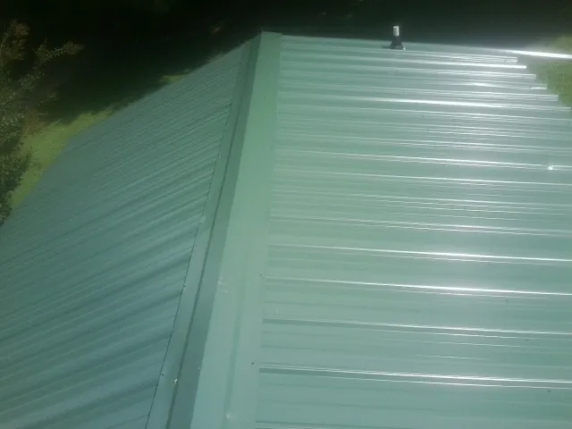 New green metal panels meeting at the ridge of a roof — Flat Roof Repair work by our crew in Blodgett