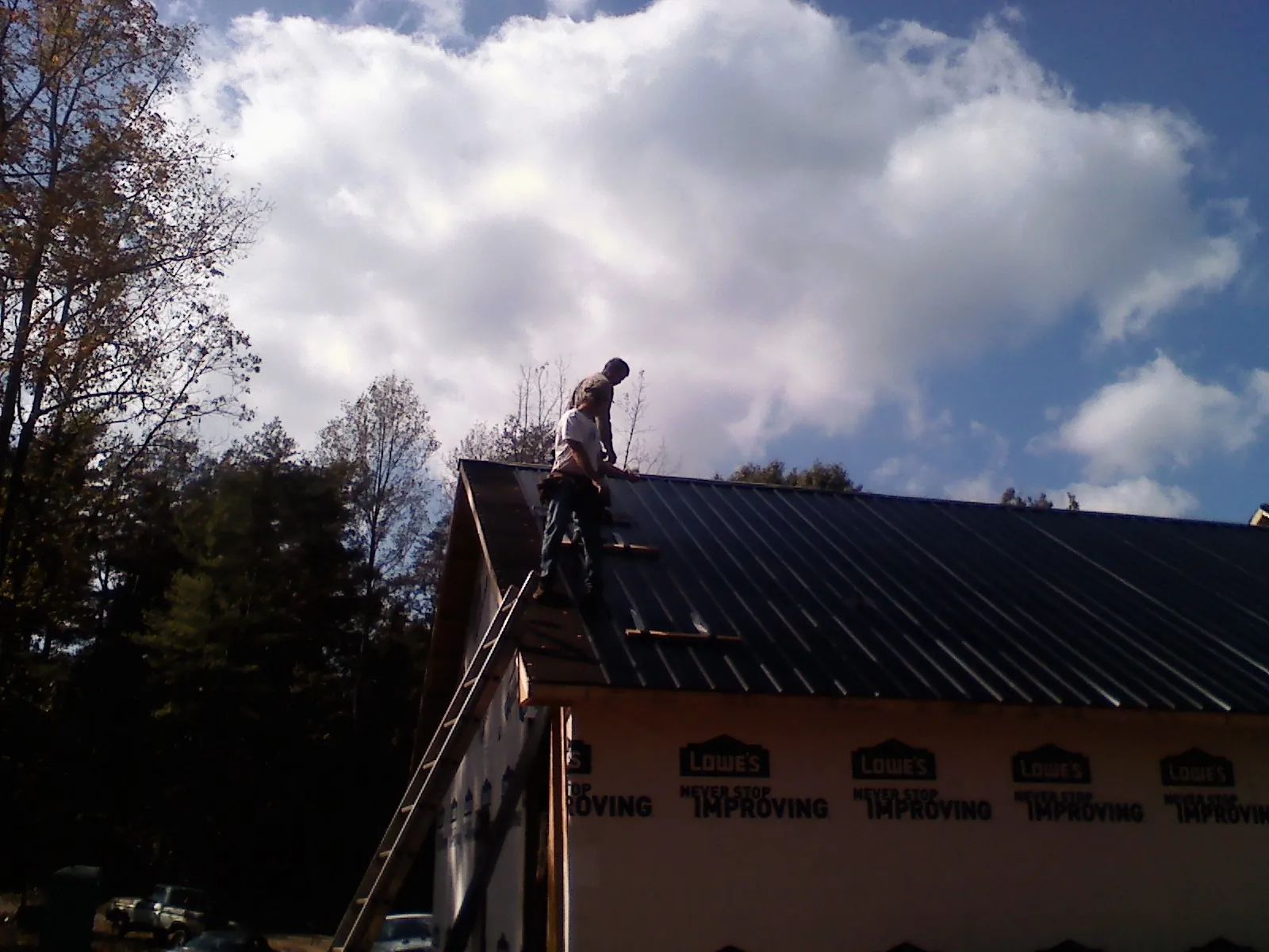 Roofer fastening dark metal panels high against a cloudy sky, from a Roof Inspection job in Blodgett