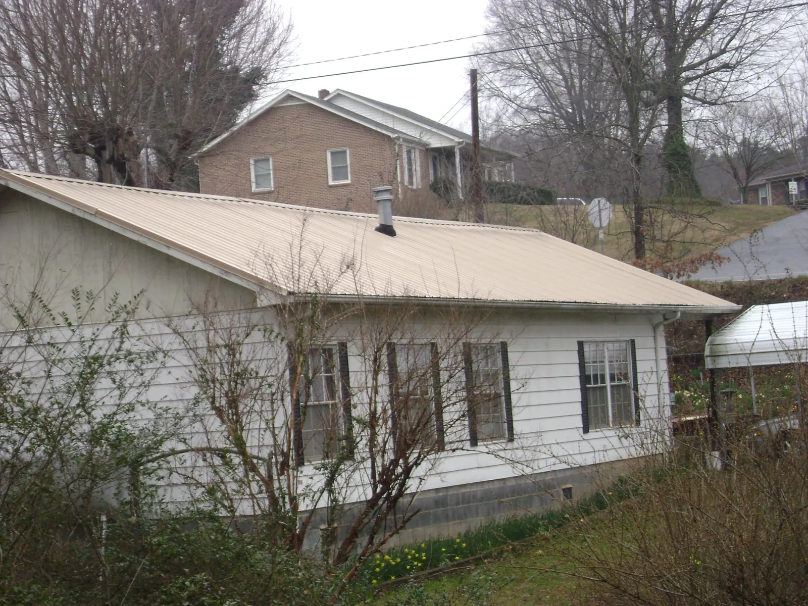 Tan metal roof on a white sided house set into a hillside — Commercial Roofing by Roofing Brothers in Blodgett