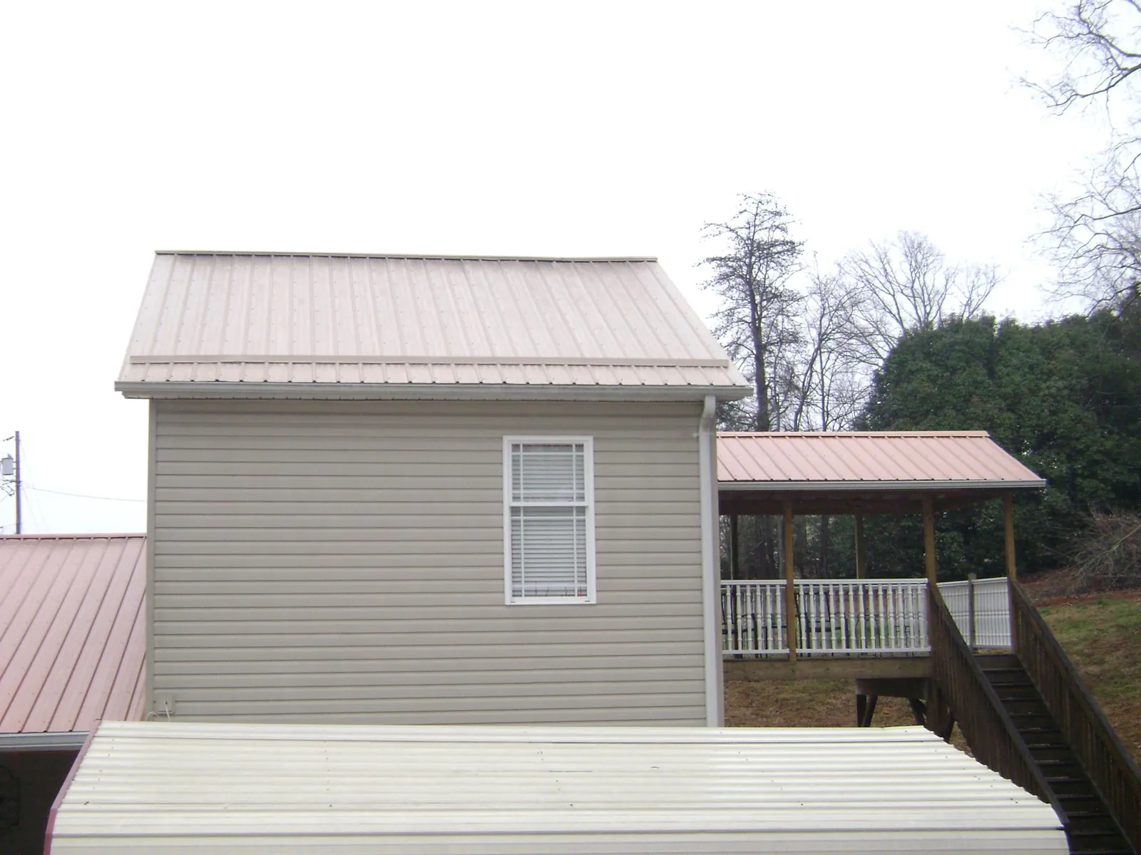 Tan metal roofs on a two story addition and attached porch, from a Roof Replacement job in Blodgett