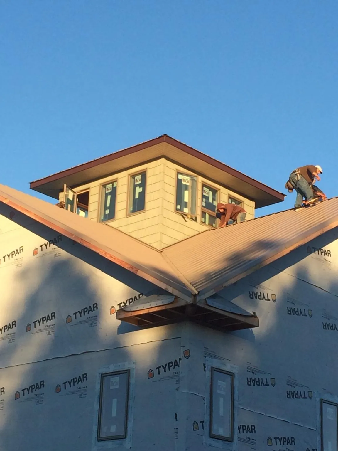 Roofers working around a rooftop cupola on a new metal roof at sunset — Roof Waterproofing in Blodgett by Roofing Brothers